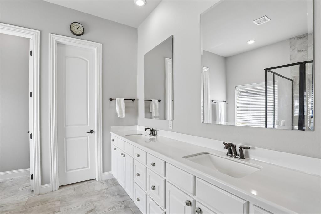 Primary bath featuring dual-sink vanity with white cabinetry, light-toned countertop, rectangular undermount sinks, oil-rubbed bronze faucets, and oversized frameless wall-mounted mirrors