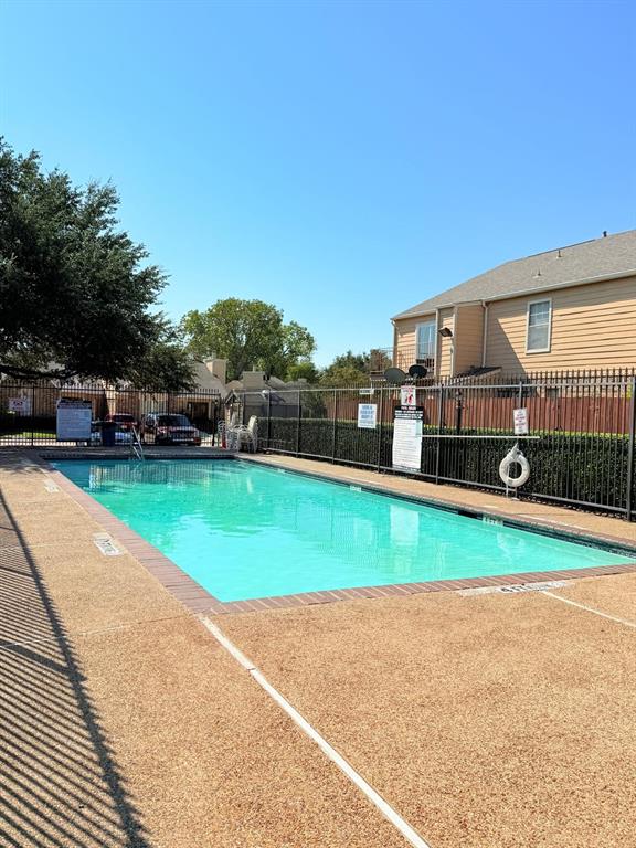 Rectangular swimming pool featuring a textured stone-aggregate pool deck, perimeter metal fencing, and brick coping