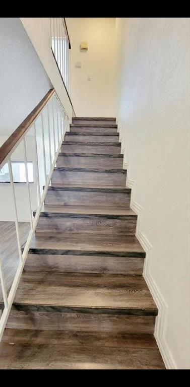 Staircase featuring wood-finish treads, a white metal railing with a stained wood handrail, and applied wall molding