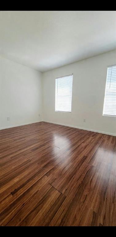 Interior space featuring wood-finish flooring, neutral walls, and dual windows with horizontal blinds