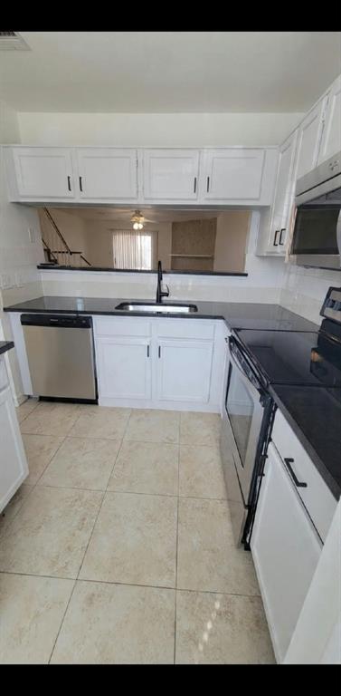 Kitchen featuring white cabinetry, dark stone-finish countertops, stainless steel appliances, tile flooring, and a matte black faucet