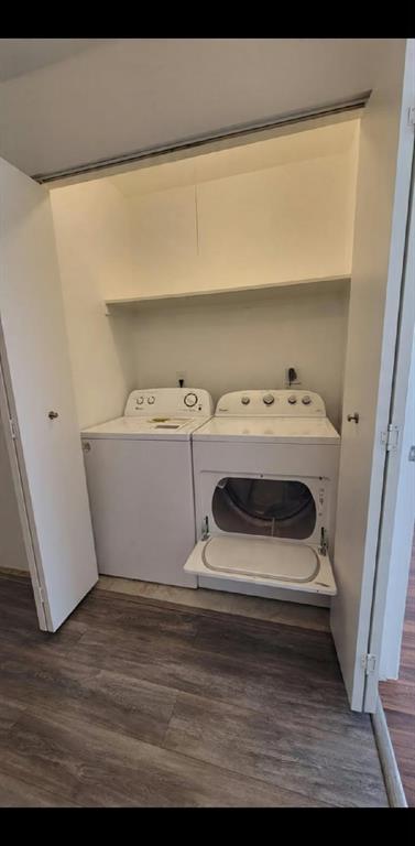 Laundry closet featuring wood-finish flooring, side-by-side washer and dryer, and an integrated overhead shelf