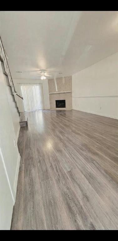 Living area featuring wood-finish flooring, a corner fireplace with a stone-finish surround, chair rail molding, and a ceiling fan