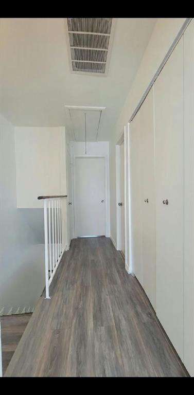 Hallway featuring wood-finish flooring, white paneled doors, ceiling-height built-in storage closets, and a white vertical-spindle railing