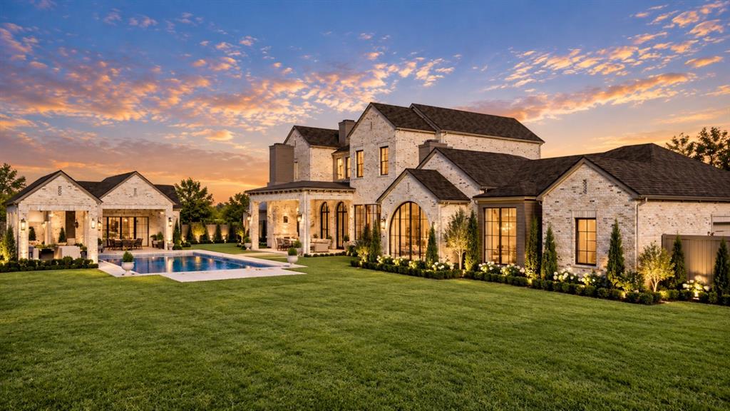 Light-colored brick exterior featuring an expansive rear lawn, an in-ground swimming pool with stone surround, a covered patio with arched entries, and large multi-pane windows