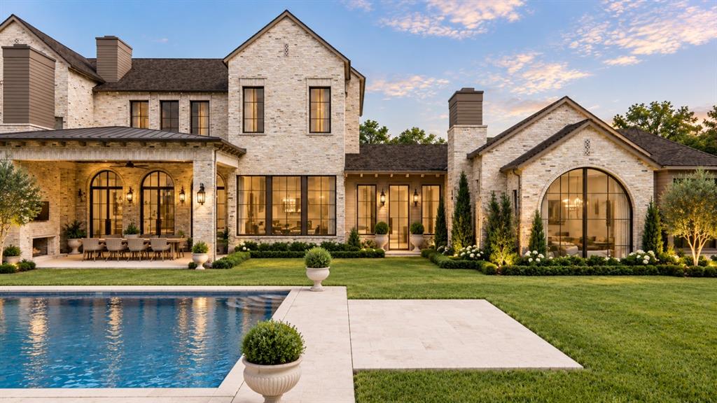 Custom stone exterior featuring a covered patio, expansive swimming pool, large arched windows, and multi-gabled roofline