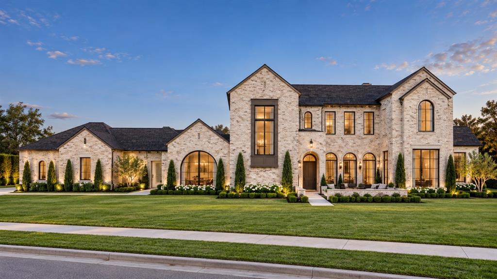Custom masonry exterior with light-toned brick, arched window detailing, steeply pitched gabled rooflines, large-format metal-framed windows, and manicured front lawn landscaping