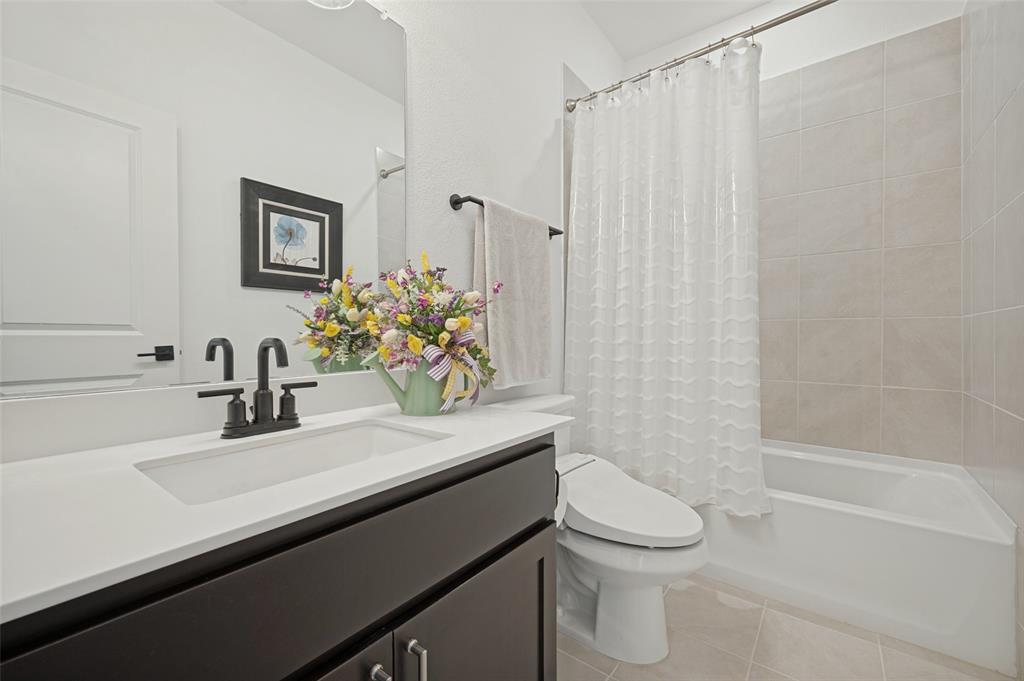 Dark-toned vanity with a rectangular sink, crisp white countertop, matte black faucet, and a tub-shower combination featuring neutral wall tiling