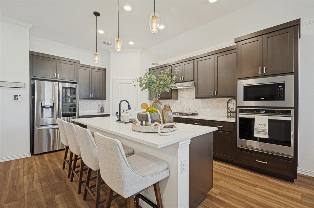Kitchen featuring dark-finish cabinetry, quartz countertops, a central island, wood-finish flooring, and stainless steel built-in appliances Kitchen featuring dark-finish cabinetry, quartz countertops, a central island, wood-finish flooring, and stainless steel built-in appliances