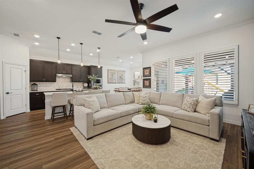 Open-concept living space featuring wood-finish flooring, recessed lighting, and a kitchen equipped with dark cabinetry and a central island Open-concept living space featuring wood-finish flooring, recessed lighting, and a kitchen equipped with dark cabinetry and a central island