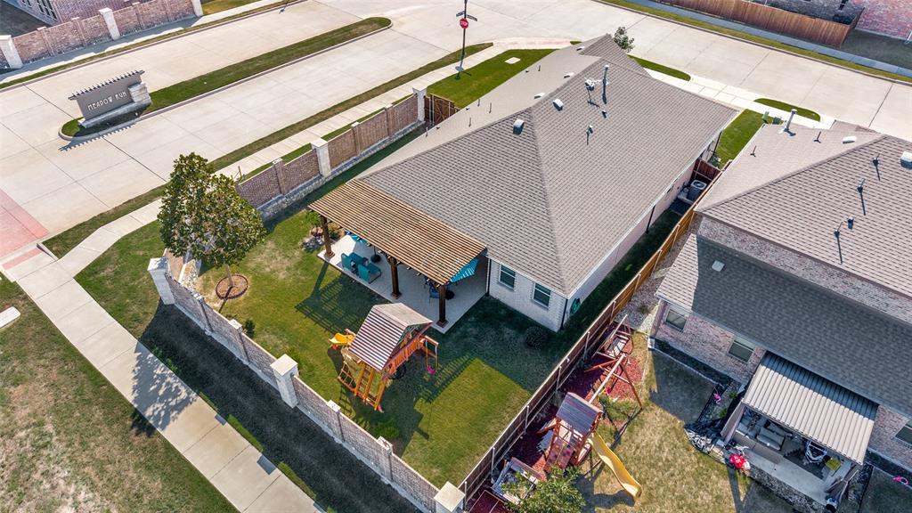 Aerial perspective of a corner lot property featuring a stone and brick perimeter wall, a covered patio with a wooden pergola, and a private lawn area