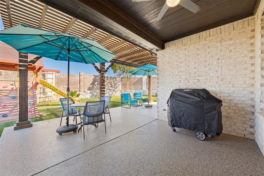Covered outdoor patio featuring a textured concrete floor, wooden pergola ceiling, white brick wall, and a ceiling-mounted fan