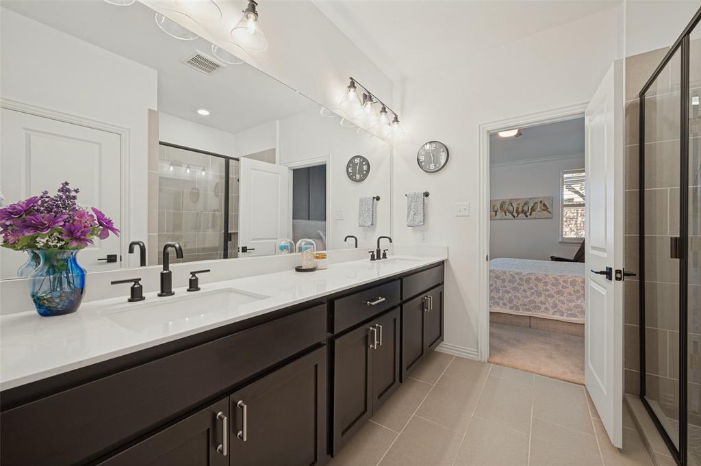 Dual-sink vanity with matte black fixtures, crisp white countertop, expansive wall-to-wall mirror, and glass-enclosed shower with neutral-toned tiling