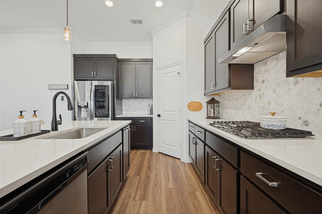 Kitchen featuring dark cabinetry, solid-surface countertops, a geometric-pattern backsplash, gas cooktop, and wood-finish flooring Kitchen featuring dark cabinetry, solid-surface countertops, a geometric-pattern backsplash, gas cooktop, and wood-finish flooring