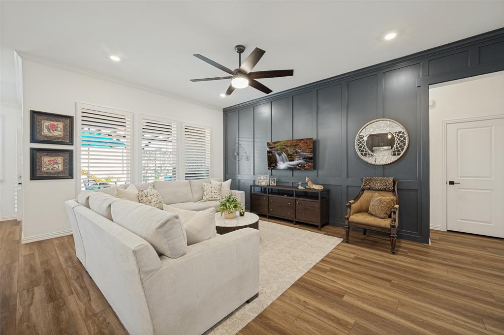 Living area featuring a floor-to-ceiling dark-toned board and batten accent wall, wood-finish flooring, recessed lighting, and a modern multi-blade ceiling fan Living area featuring a floor-to-ceiling dark-toned board and batten accent wall, wood-finish flooring, recessed lighting, and a modern multi-blade ceiling fan