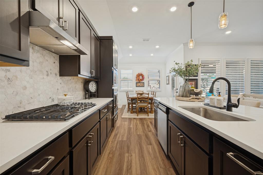 Kitchen featuring dark cabinetry, quartz countertops, a stone-tile backsplash, stainless steel gas cooktop, and wood-finish flooring Kitchen featuring dark cabinetry, quartz countertops, a stone-tile backsplash, stainless steel gas cooktop, and wood-finish flooring