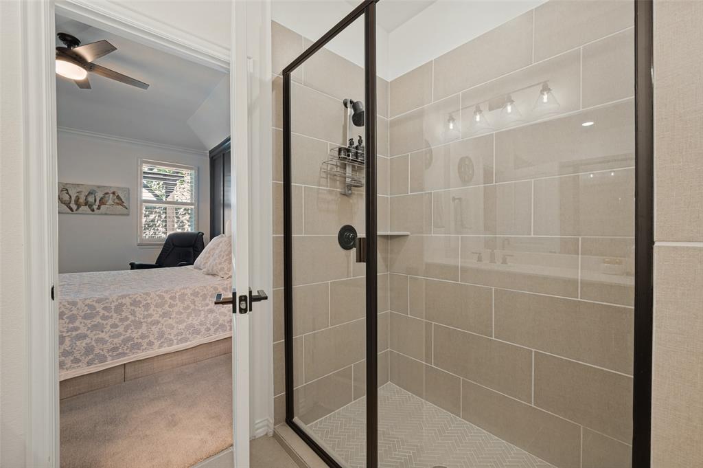 Walk-in shower featuring large-format beige wall tile, herringbone-patterned floor tile, matte black hardware, and a glass enclosure with a black frame