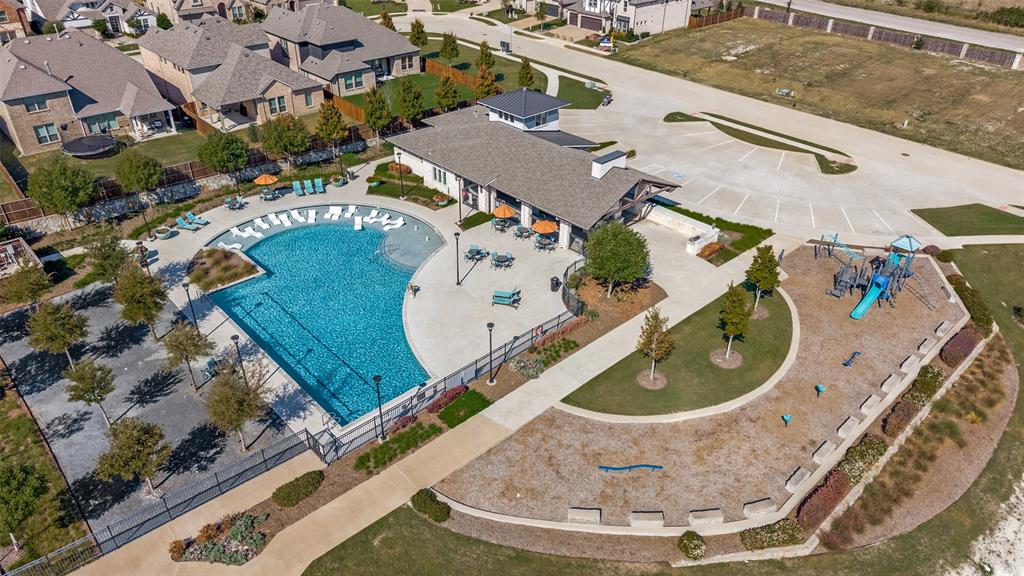 Community amenity center featuring a swimming pool with a shallow sun shelf, expansive concrete decking, a covered pavilion, and a playground with mulch surfacing