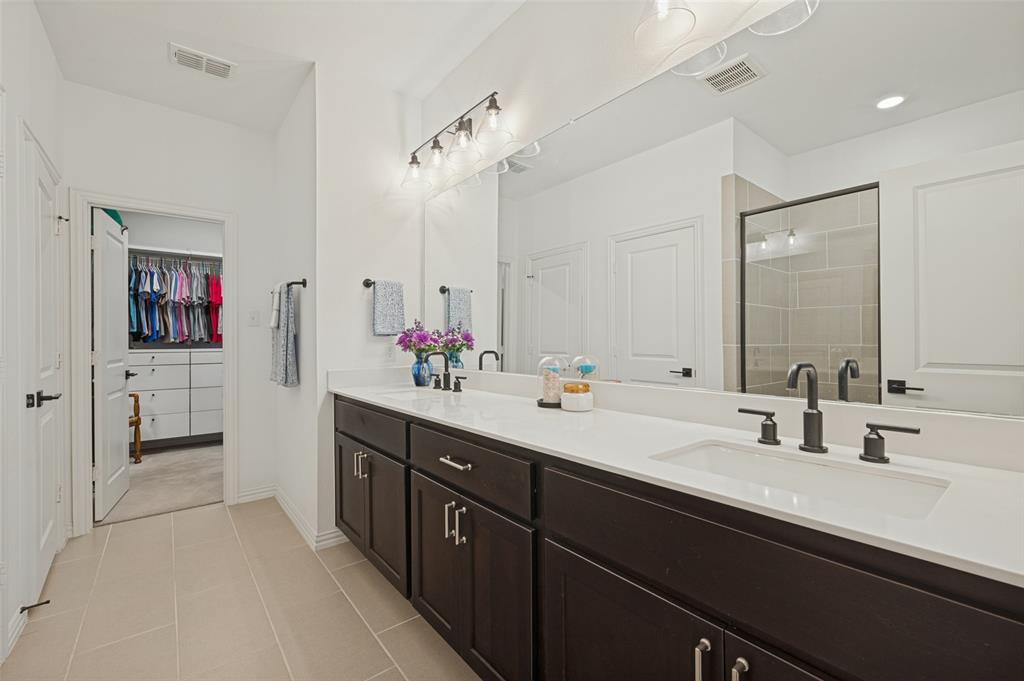 Double vanity featuring dark cabinetry, solid-surface white countertops, rectangular undermount sinks, matte black widespread faucets, and a full-width mirror