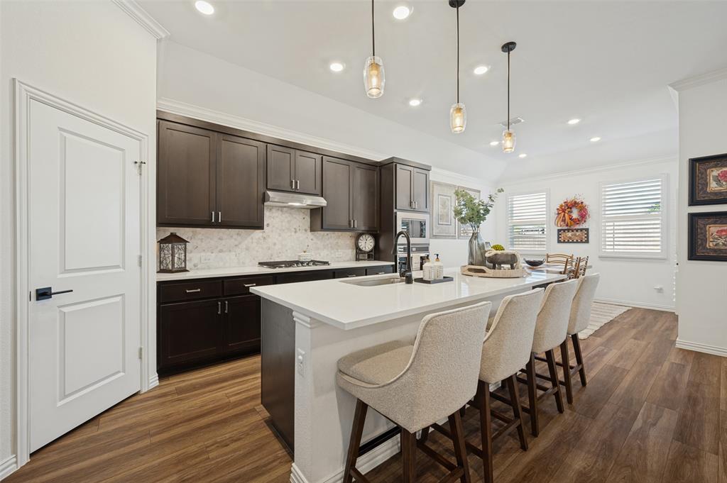 Kitchen featuring dark wood cabinetry, quartz countertops, a stone-patterned backsplash, wood-finish flooring, and pendant lighting Kitchen featuring dark wood cabinetry, quartz countertops, a stone-patterned backsplash, wood-finish flooring, and pendant lighting
