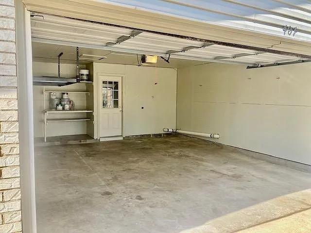 Two-car garage featuring a concrete floor, built-in shelving, overhead door mechanism, and a separate entry door with a windowed panel
