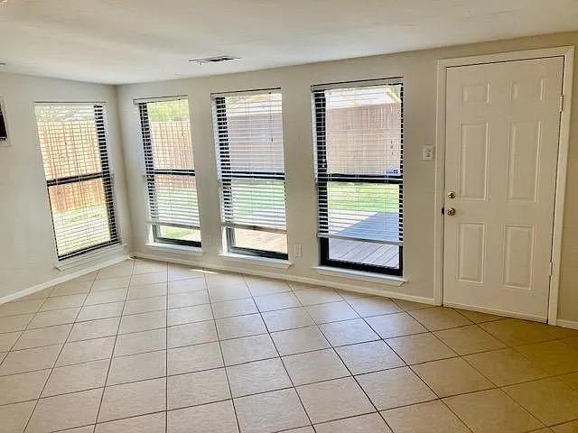 Neutral tile flooring, multiple windows with horizontal blinds, and a paneled exterior access door Neutral tile flooring, multiple windows with horizontal blinds, and a paneled exterior access door