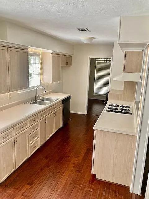 Kitchen featuring light-finish cabinetry, wood-finish flooring, solid-surface countertops, a dual-basin stainless steel sink, and a built-in gas cooktop Kitchen featuring light-finish cabinetry, wood-finish flooring, solid-surface countertops, a dual-basin stainless steel sink, and a built-in gas cooktop