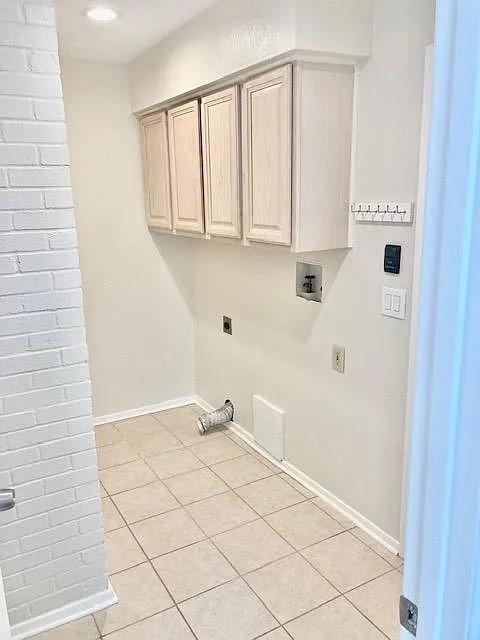 Utility room featuring ceramic tile flooring, painted brick wall detail, and upper cabinetry for storage