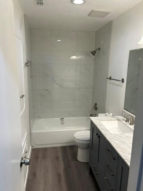 Bathroom featuring wood-finish flooring, a charcoal gray vanity with a light-toned countertop, and a tub-shower combination finished with large-format tile surround Bathroom featuring wood-finish flooring, a charcoal gray vanity with a light-toned countertop, and a tub-shower combination finished with large-format tile surround