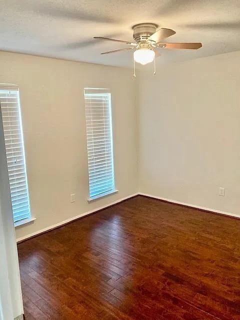 Room featuring wood-finish flooring, two windows with horizontal blinds, and a ceiling fan with integrated lighting