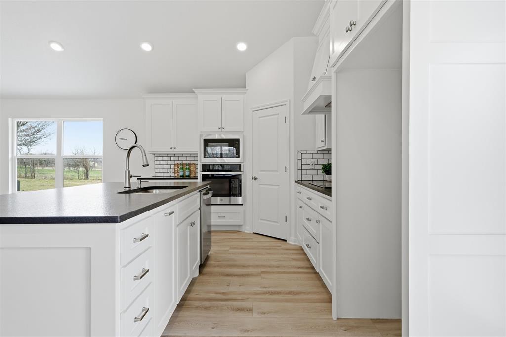 Kitchen featuring white shaker-style cabinetry, dark stone countertops, stainless steel wall-mounted oven and microwave, subway tile backsplash, and wood-finish flooring