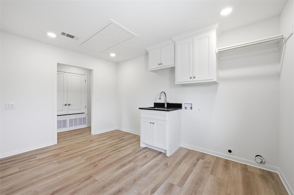 Laundry room featuring wood-finish flooring, shaker-style cabinetry, a stone-finish countertop with a drop-in basin, and a wall-mounted hanging rack