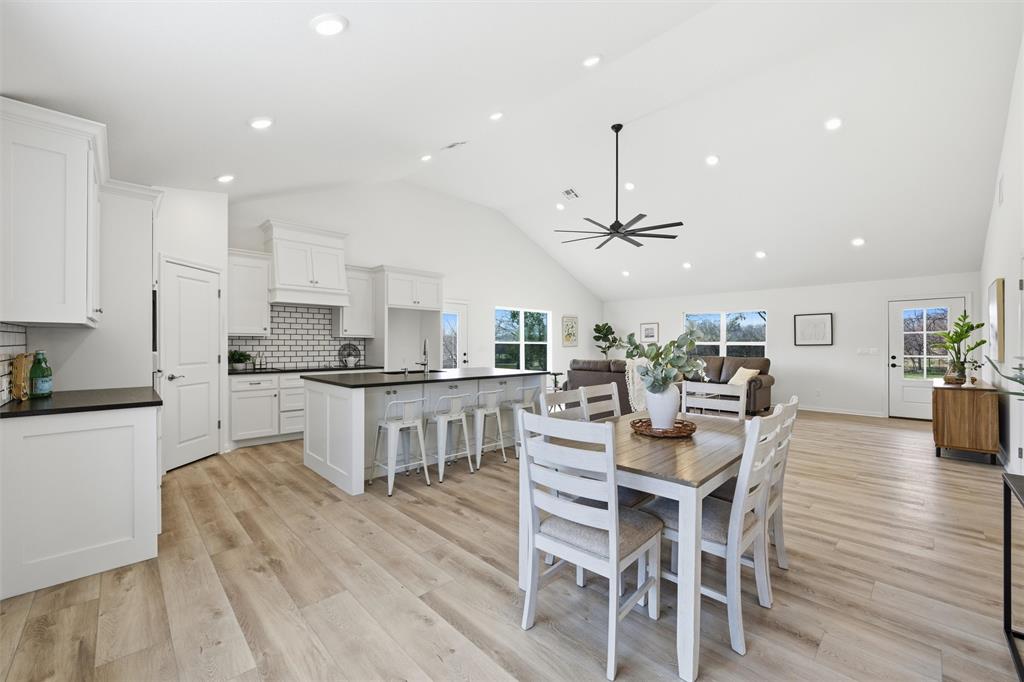 Open-concept kitchen and living area featuring vaulted ceilings, recessed lighting, wood-finish flooring, a central island with countertop seating, and a subway tile backsplash