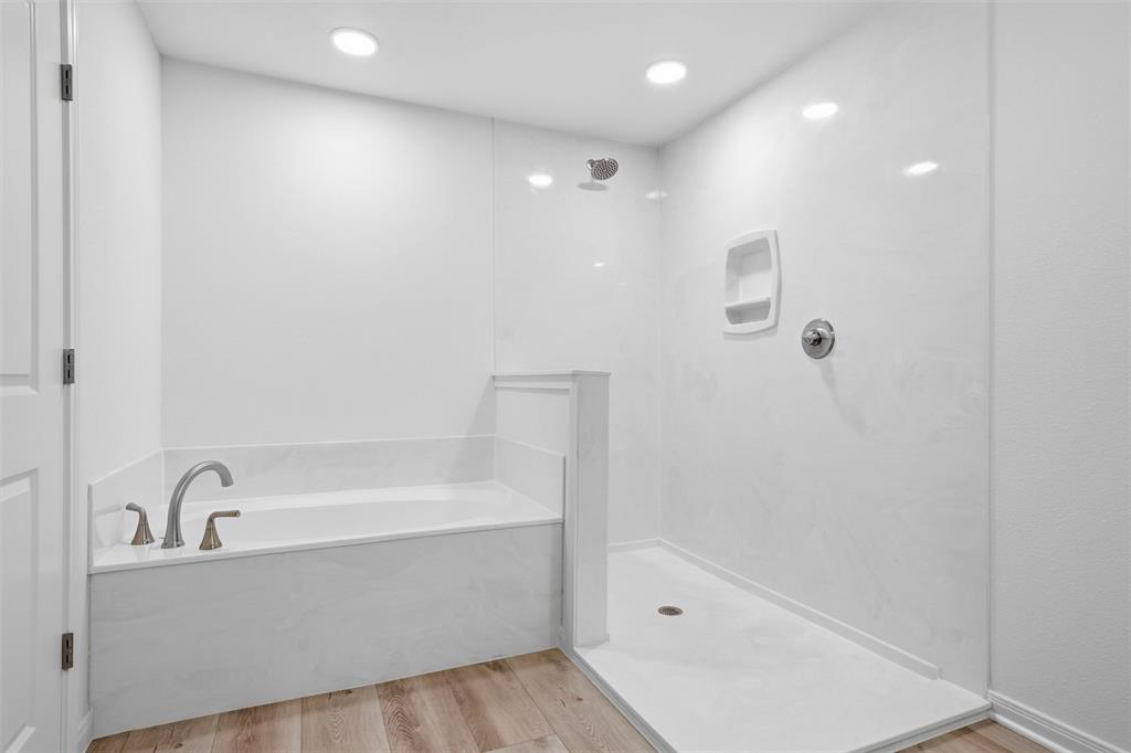 Soaking tub with a curved faucet, separate walk-in shower featuring a built-in recessed soap niche, light-toned wood-finish flooring, and recessed ceiling lighting