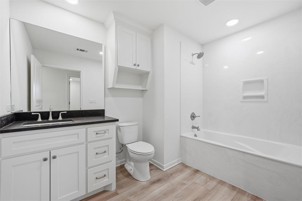 Bathroom featuring white cabinetry, dark stone countertop, integrated sink, wood-finish flooring, and a tub-shower combination with an inset wall niche