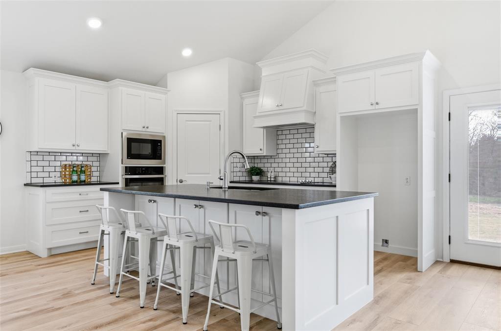 Kitchen featuring white shaker-style cabinetry, dark stone countertops, subway tile backsplash, a center island with undermount sink, and recessed lighting