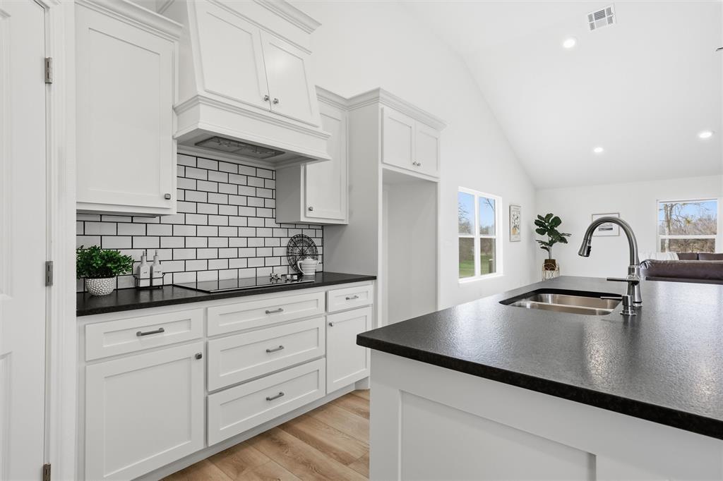Kitchen featuring white shaker-style cabinetry, a contrasting dark countertop, subway tile backsplash, vaulted ceilings, and a central island with an undermount sink