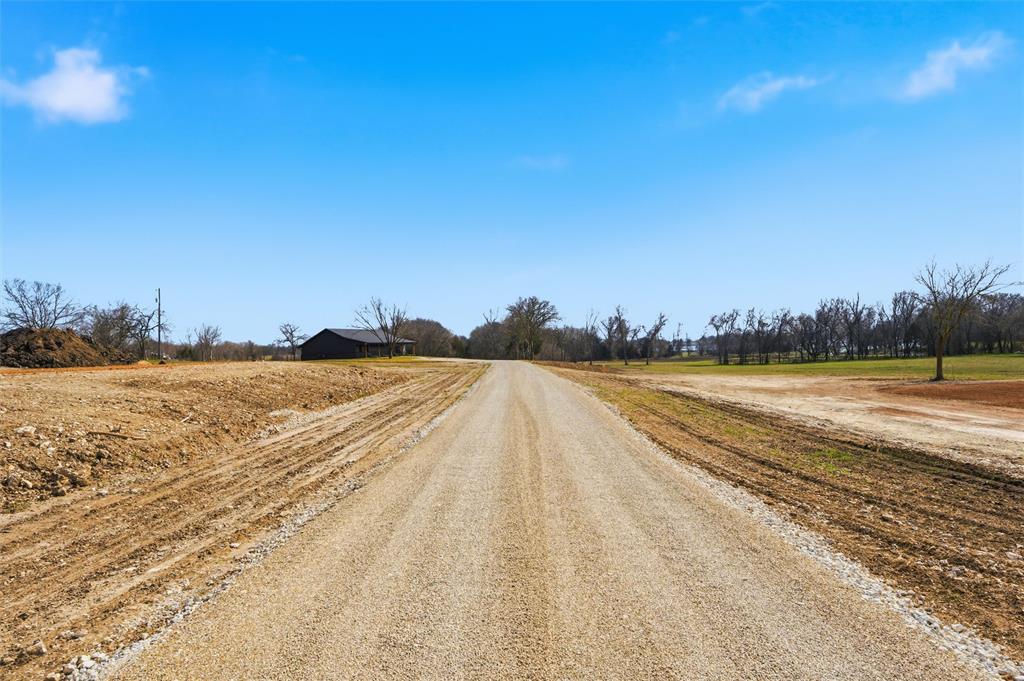 Expansive cleared acreage featuring a gravel road, level topography, and mature trees
