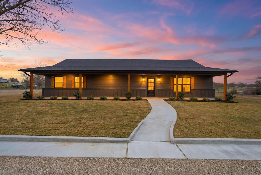 Single-story exterior featuring dark horizontal siding, a full-length covered porch with timber support beams, and a concrete walkway Single-story exterior featuring dark horizontal siding, a full-length covered porch with timber support beams, and a concrete walkway