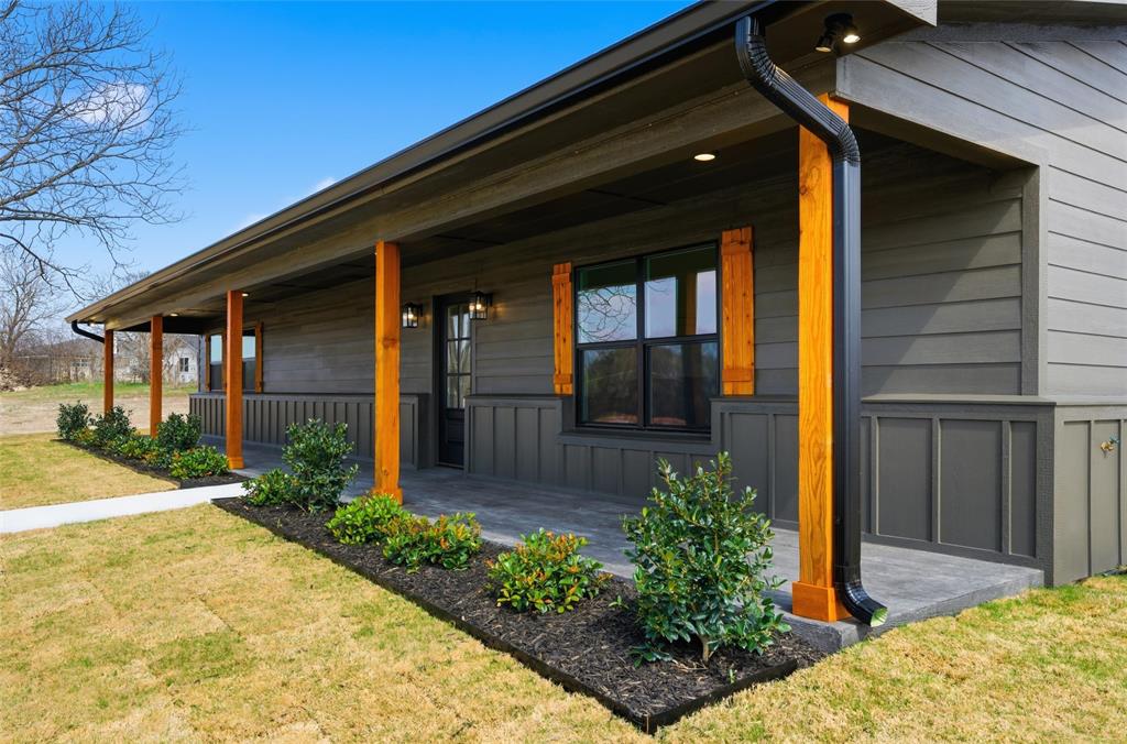 Exterior featuring board-and-batten and lap siding, a covered porch with natural wood support posts, dark-toned window shutters, and integrated recessed lighting Exterior featuring board-and-batten and lap siding, a covered porch with natural wood support posts, dark-toned window shutters, and integrated recessed lighting