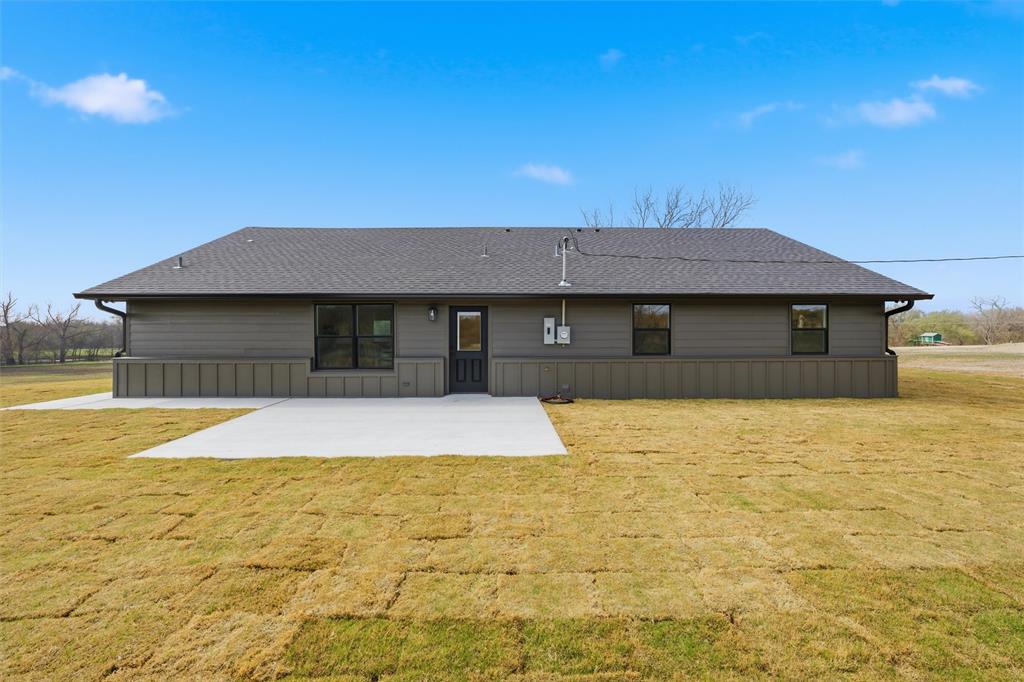 Exterior rear facade featuring dark-toned siding, a combination of board-and-batten and horizontal paneling, a gabled roofline, and a poured concrete patio