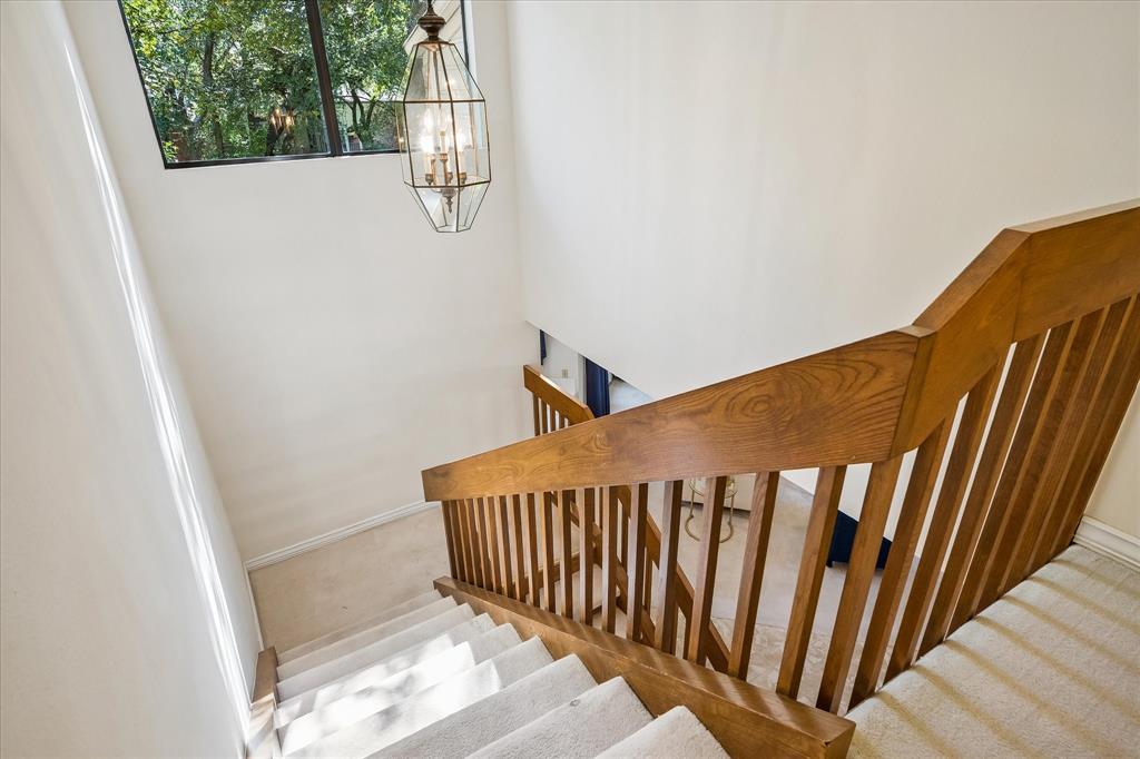 View from the top of the wooden staircase with a large window bringing in natural light into the home and a nice light fixture.
