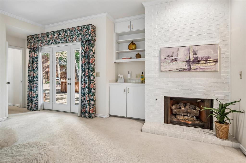 Another view of the primary bedroom with built-ins and a gas log fireplace providing ambiance to the room.  The door leads to the spacious outdoor deck providing spectacular views of the large backyard creek lot.