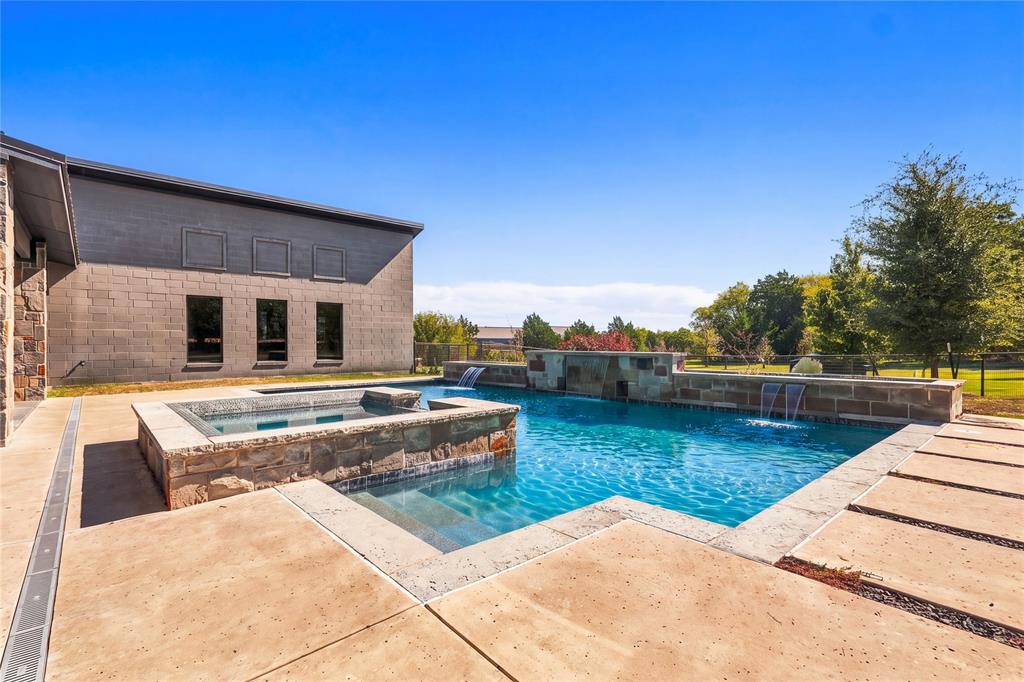 In-ground swimming pool featuring a stacked-stone spa, cascading water features, and expansive concrete hardscaping