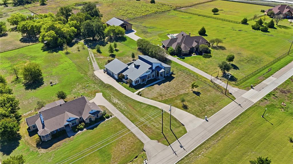 Aerial perspective of a multi-structure property featuring expansive pasture land, multiple concrete driveways, a detached storage building, and fenced perimeter boundaries Aerial perspective of a multi-structure property featuring expansive pasture land, multiple concrete driveways, a detached storage building, and fenced perimeter boundaries