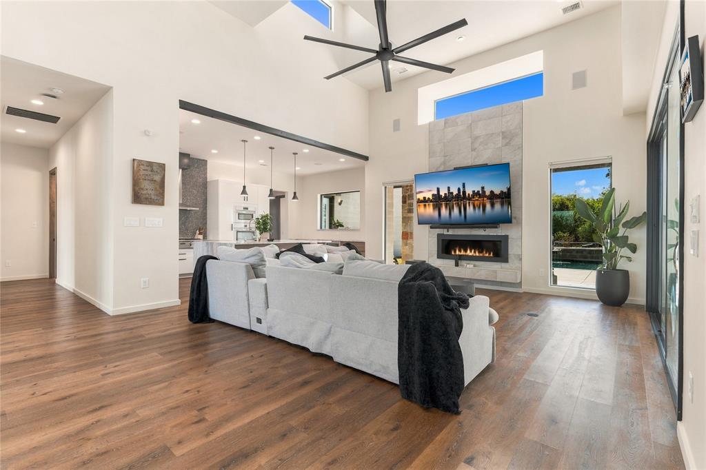 Vaulted ceilings with transom windows, stone-clad gas fireplace, wood-finish flooring, recessed lighting, and multi-panel sliding glass doors Vaulted ceilings with transom windows, stone-clad gas fireplace, wood-finish flooring, recessed lighting, and multi-panel sliding glass doors