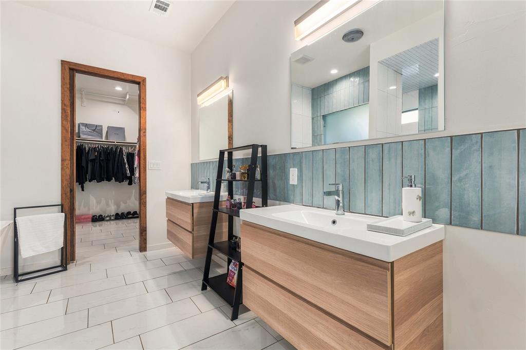 Dual wall-mounted wooden vanities featuring white rectangular sinks, vertical blue ceramic tile backsplash, integrated lighting, and tile flooring