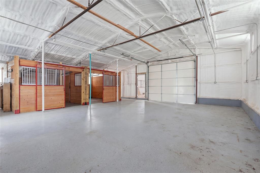 Interior structure featuring sprayed foam insulation, wood-paneled stalls with metal grating, concrete flooring, and a large metal overhead door