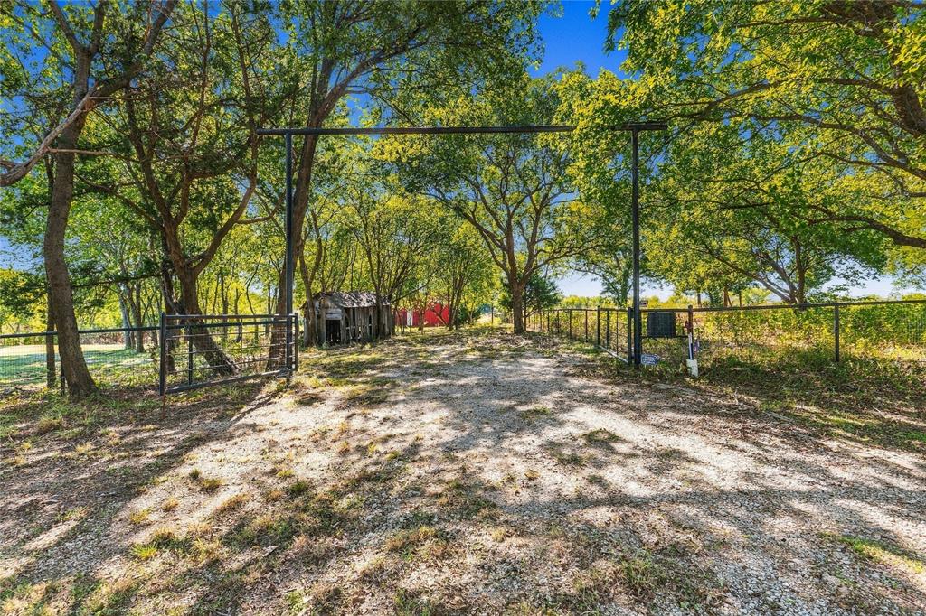 Gravel driveway entrance featuring metal pipe fencing, a steel gate, and mature trees