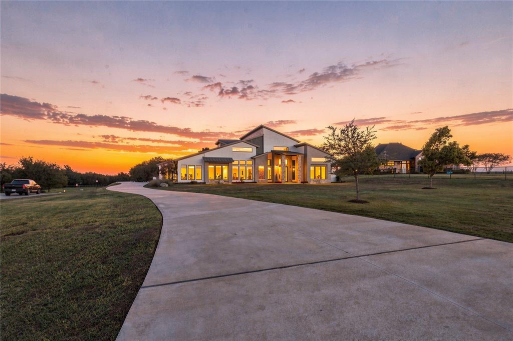 Contemporary residence featuring a multi-gabled roofline, stone and stucco exterior, expansive windows, and a paved private driveway set on a landscaped lot